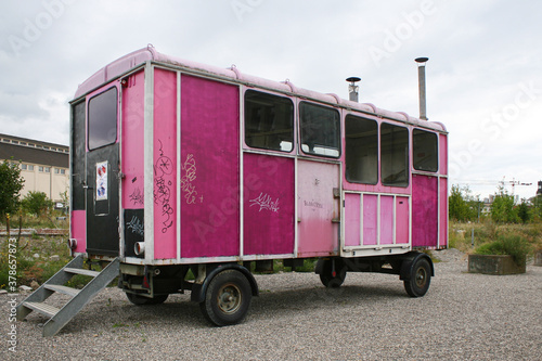 An old, broken-down caravan truck, with its panels painted several different colours of pink, under a flat grey sky.  Image has copy space. © Dana