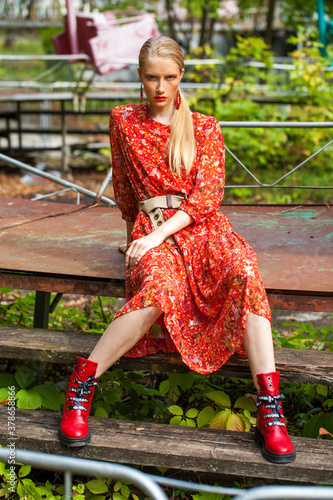 Young beautiful blonde woman in a bright red dress posing sitting, autumn park outdoors