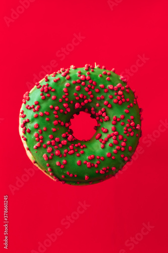 green christmas donut with red sprinkle isolated on red backround. holiday, celebration concept. vertical orientation.