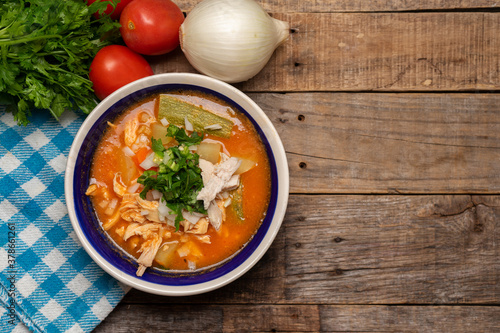 Mexican chicken soup with vegetables and rice on wooden background