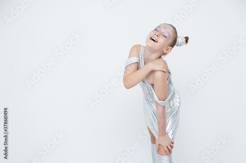 girl in a silver dress leans on her leg with her eyes closed and smiles.