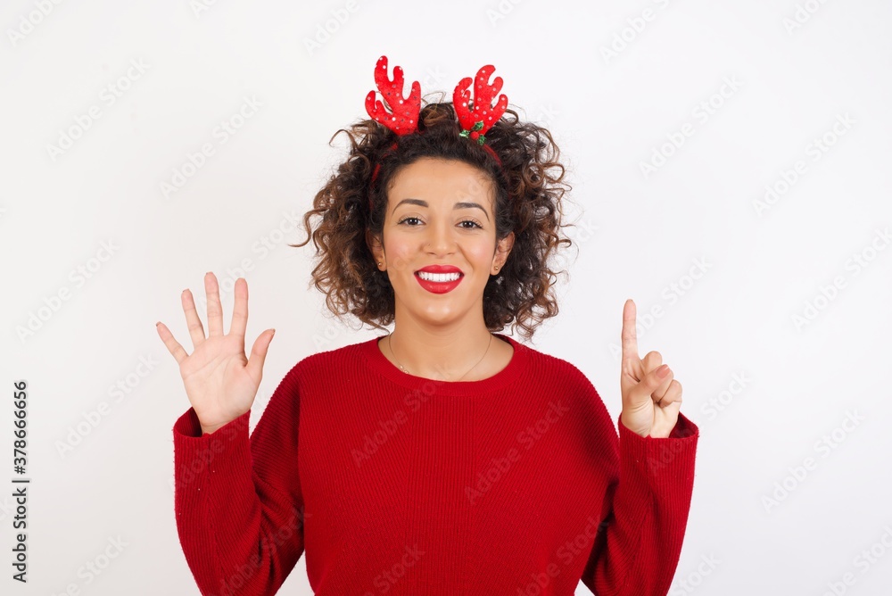 Young arab woman with curly hair wearing christmas headband standing on white background showing and pointing up with fingers number six while smiling confident and happy. Young arab woman with curly hair wearing christmas headband standing on white background showing and pointing up with fingers number six while smiling confident and happy.