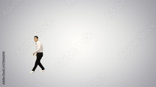 Young man in white shirt doing back flip looking at camera and walking away on gradient background.