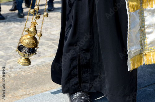 A priest swings a thurible on missal. Orthodox priest with hand censer during worship service. Censer used during liturgy. Man swinging chain censer. 