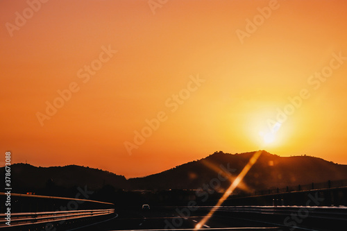 Scenic view of orange sky picturesque sunset and highway with single car drivingon it on a way to mountains silhouette. © Mila