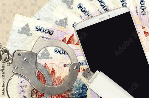 1000 Cambodian riels bills and smartphone with police handcuffs. Concept of hackers phishing attacks, illegal scam or malware soft distribution photo