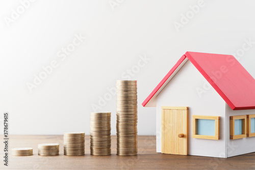 Money and miniature house. Finance and investment. Miniature house and stack of coins on wood table.