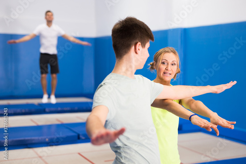 Experienced female trampoline instructor teaching teenage boy of right technique in sports center..