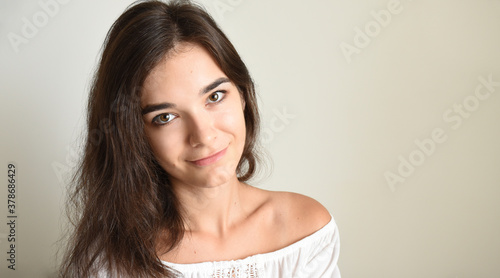 Portrait of young 25 y.o. brunette Russian woman with long hair. In white open shoulder top and looking into the camera on light gray background. Minimum makeup, natural hairstyle. copy space