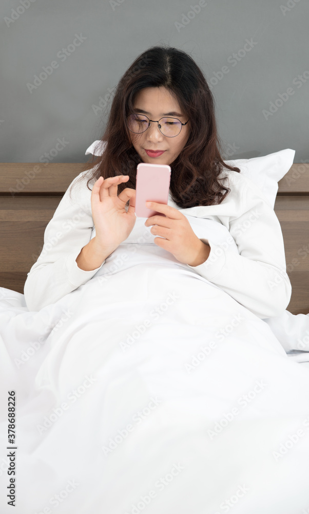 Oriental lady happily playing with mobile phone in bedroom Oriental lady happily playing with mobile phone in bedroom