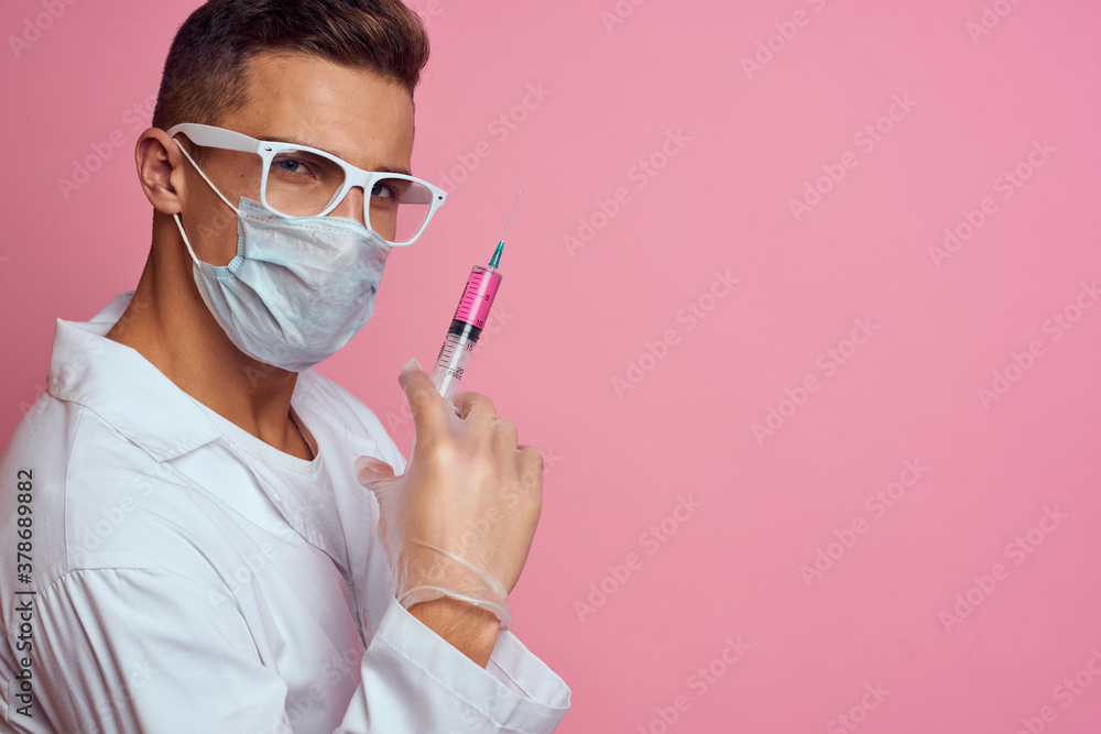 A doctor in a medical mask and gloves holds a syringe in the hands of an injection laboratory