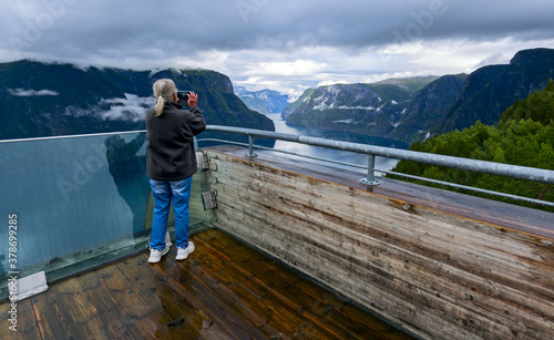 enderly woman photographing on spectacular Stegastein viewing platform above Aurlandsfjord. It is located on national tourist route Aurlandsfjellet. It is build with front class wall