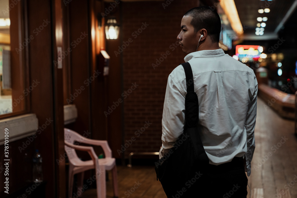 Back view - Business man wear headphone walking on street at night.