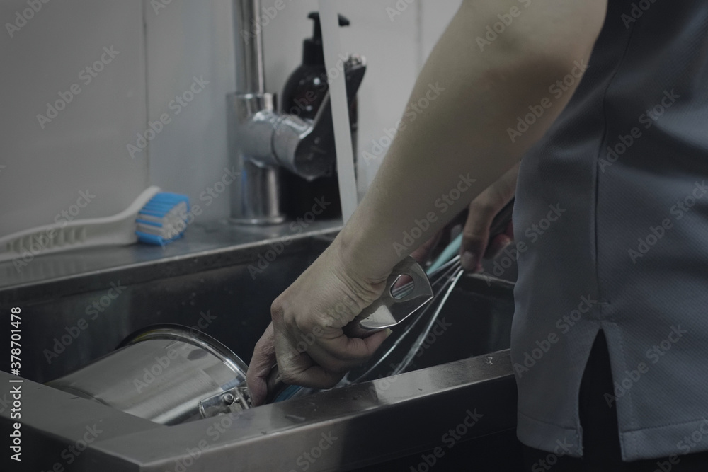 Closeup of female hands washing dishes on commercial kitchen. Unrecognizable female standing at the sink in the kitchen and wash kitchen utensil