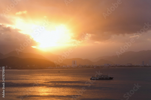 Sunset at South China Sea. Orange cloudy sky at sundown. Incredible cityscape, seascape with floating ship at beautiful golden sunset © Azhorov