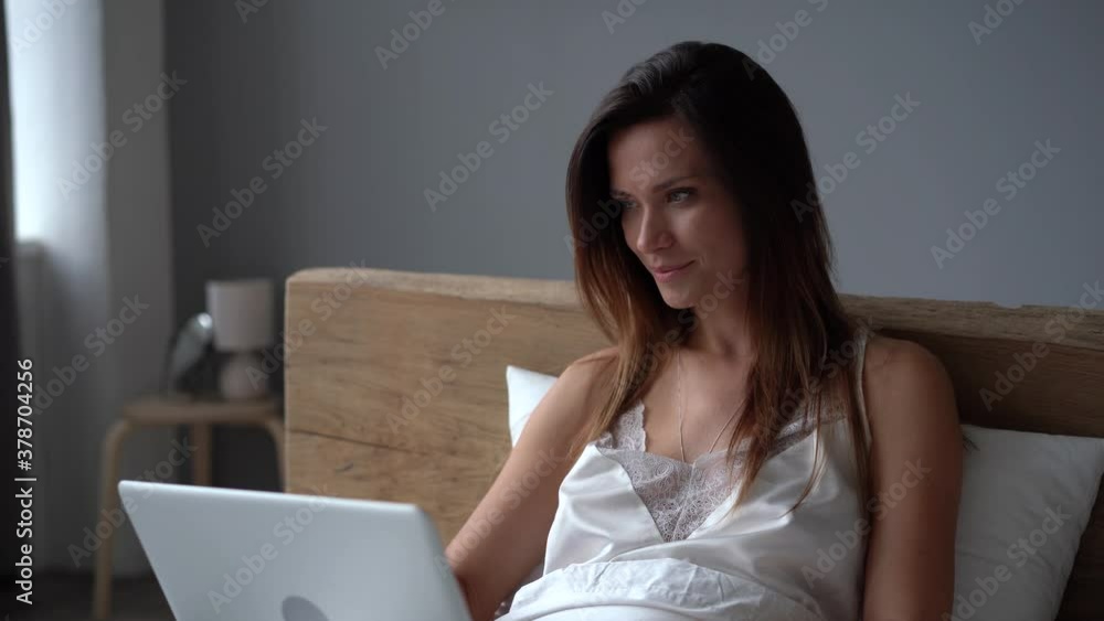 Young woman typing on laptop and sitting in bed Young woman typing on laptop and sitting in bed
