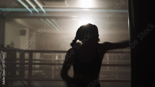 Boxing, woman fighter trains his punches, beats a punching bag, training in the boxing gym, strength fit body, the girl strikes fast, backlighting.