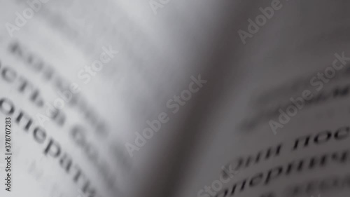 Printed lines of text consisting of words with black letters on pages of hardcover book made of white paper on fold of textbook fast movement of camera from top to bottom with variable focus close up photo