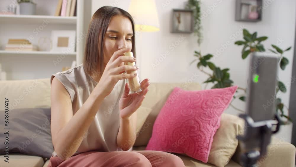 Beauty vlogger sitting on sofa in living room applying foundation on face with makeup brush on smartphone camera Beauty vlogger sitting on sofa in living room applying foundation on face with makeup brush on smartphone camera