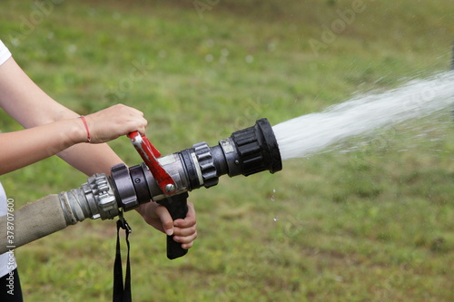Boy scout pours water a powerful fire hose close up on summer day, children emergency training photo