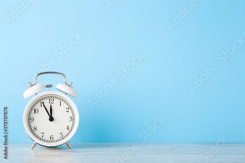 White alarm clock on wooden table at light blue wall background. Pastel color. Time concept. Closeup. Empty place for text. Front view.