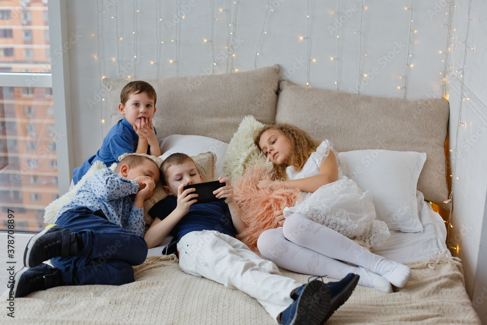 New technology. Happy little kids with mobile phone. Order gifts for Christmas and New year by phone. Small children use their smartphone in bed. Merry Christmas and happy New year greetings.