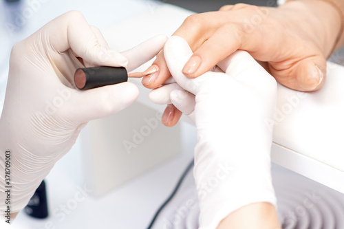 Manicure master in protective gloves applying beige nail polish on female nails in beauty salon © okskukuruza