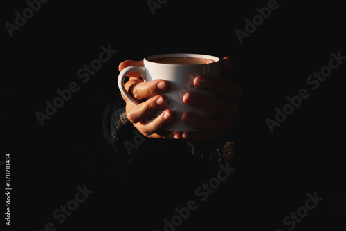 Obraz na płótnie Female hands holding white cup of coffee on black background. Woman warming her hands on mug of hot beverage in the dark. Minimal style. Copy space. Low key w salonie