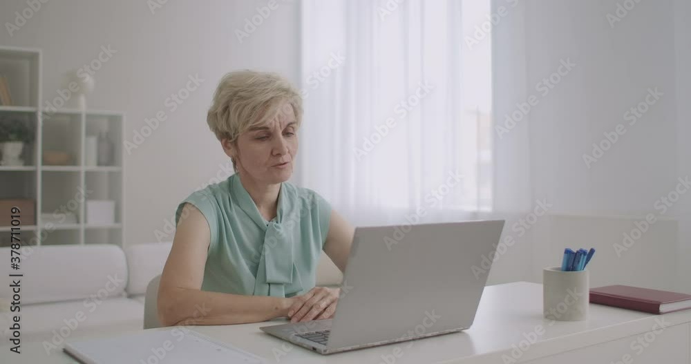 middle-aged woman is talking online by video call on notebook, sitting at home, modern technology of communication middle-aged woman is talking online by video call on notebook, sitting at home, modern technology of communication