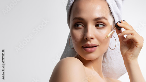 Beautiful woman in white towel with perfect skin applying moisturizing facial serum  photo
