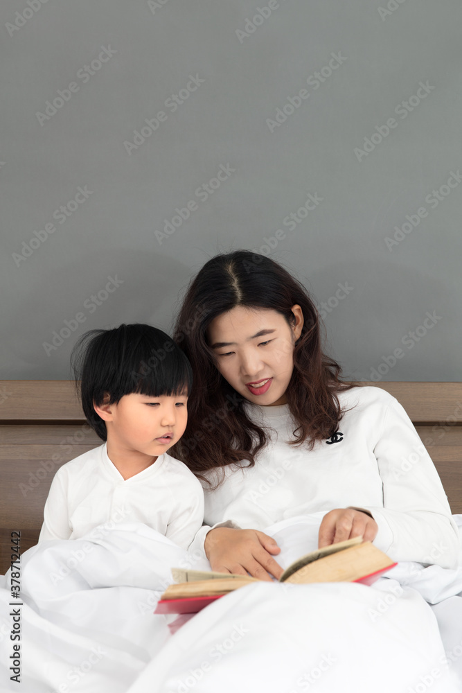 Young mother sitting on the bedside telling stories to children Young mother sitting on the bedside telling stories to children