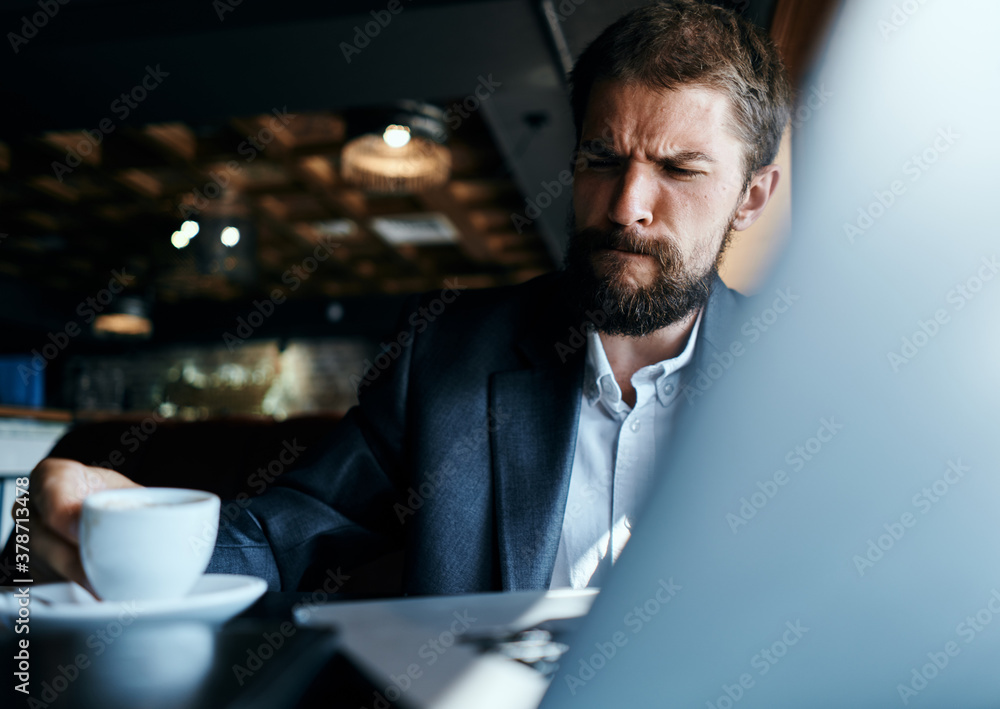 Business man sitting in a cafe with a cup of coffee in his hands in front of a laptop technology communication