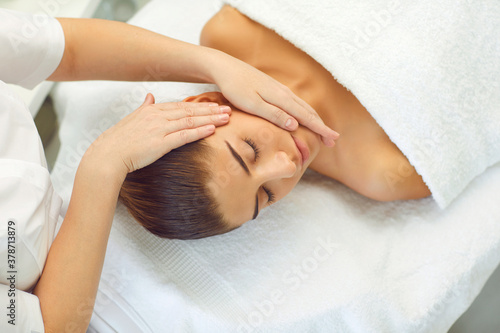 Young woman lies on a couch and receives a head massage from the hands of a masseur