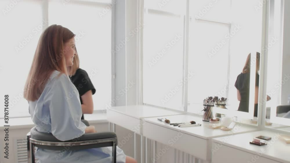 Adult makeup artist finished her work and leave away while young model enjoying her make up