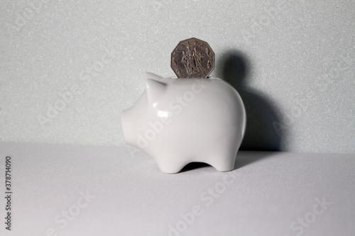 a coin from malta falls into a white piggy bank