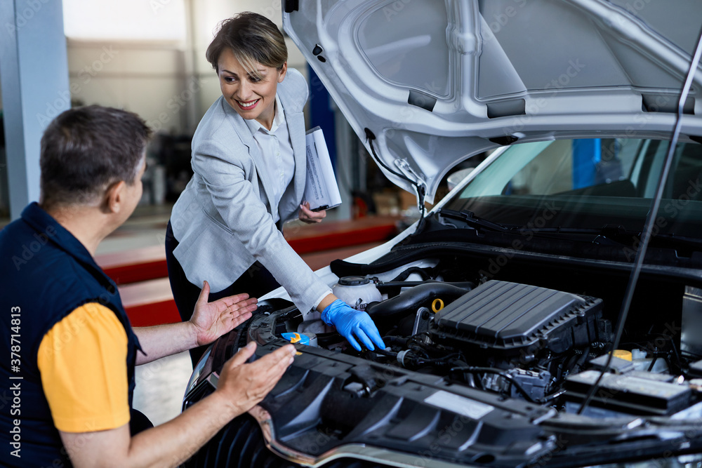 Female manager and auto mechanic examining car engine in auto repair shop. Female manager and auto mechanic examining car engine in auto repair shop.