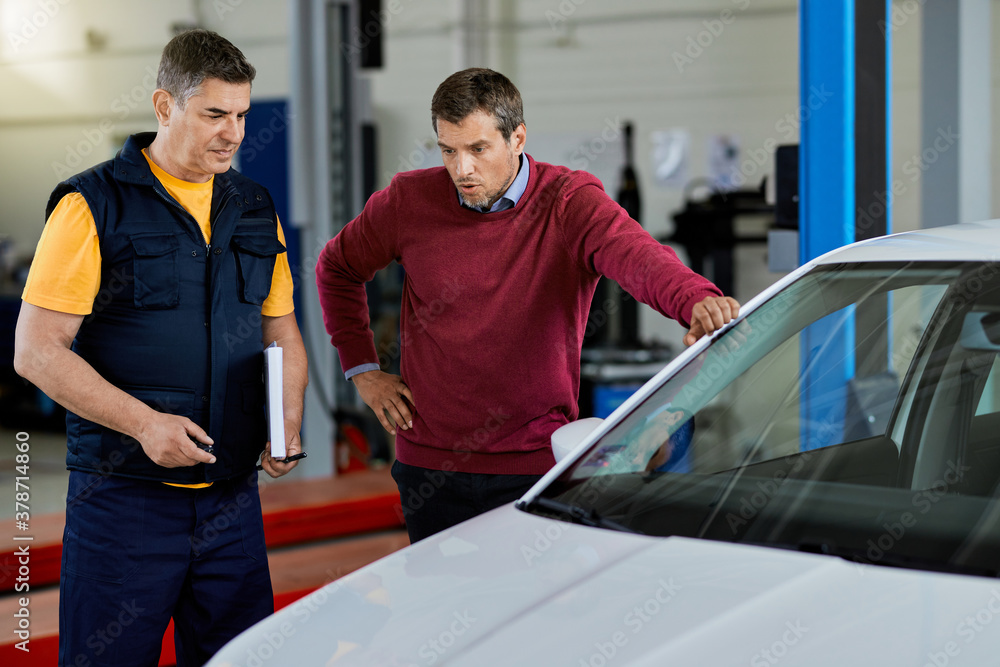 Fototapeta premium Distraught man and his mechanic in auto repair shop.
