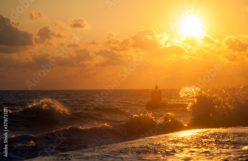 Stormy sea waves on the seashore against the pear and backdrop of the setting sun and sky with clouds.