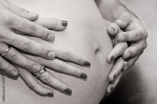 Kobieta w ciąży i męskie oraz damskie dłonie obejmujące brzuch.