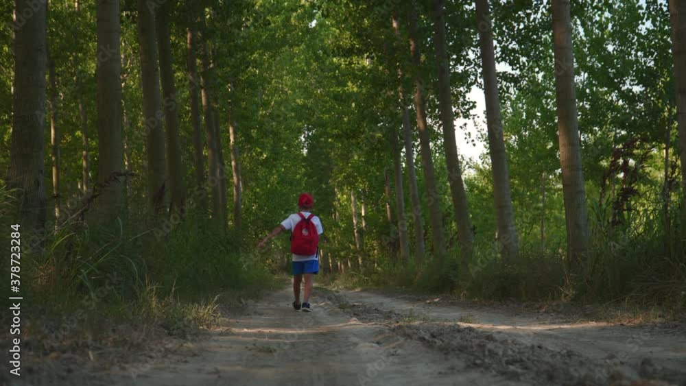a lonely kid with red bag and red hat walking down a rural road a lonely kid with red bag and red hat walking down a rural road