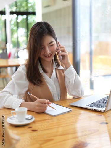 Female college student searching information on smartphone  while doing homework