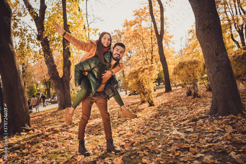 Full size photo of positive couple in fall september forest park guy hold girl piggyback wear october outerwear