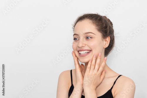 The girl smiles, touches her face with her hands.