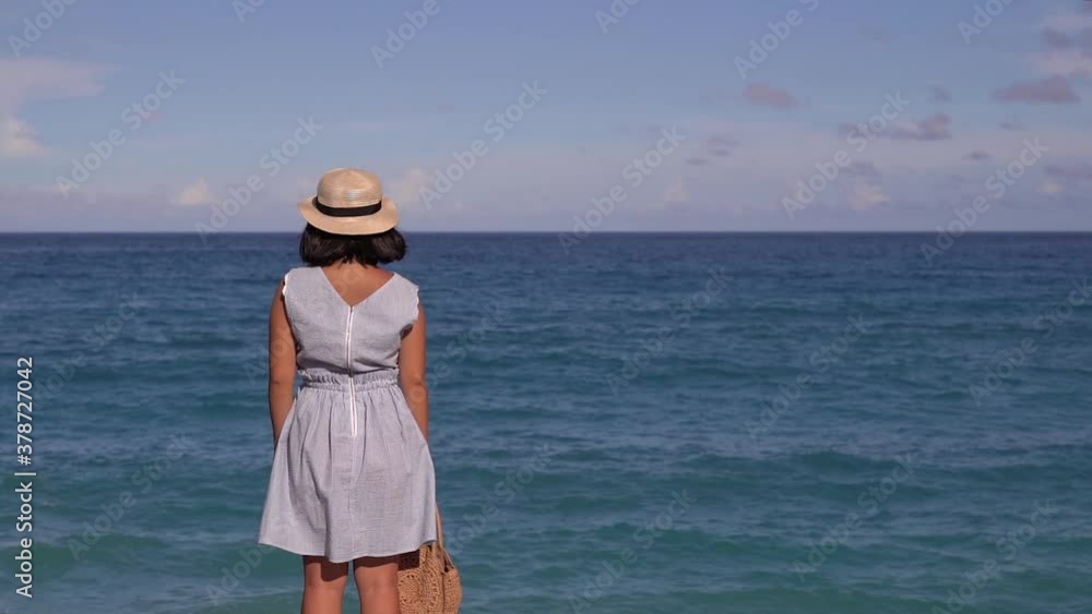Back of girl in summer dress standing in front of wide open Ocean Horizon on bright and sunny day with high waves splashing in front of her Back of girl in summer dress standing in front of wide open Ocean Horizon on bright and sunny day with high waves splashing in front of her