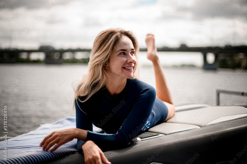 Beautiful young smiling woman with in wetsuit lies on the boat.