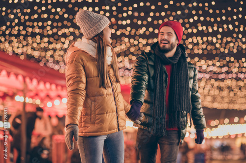 Photo of couple go walk under x-mas christmas evening outside advent illumination wear season coats