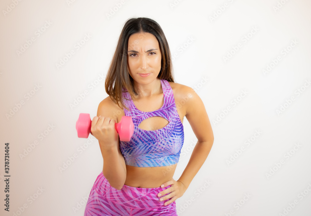 Woman in sportswear doing exercise with a pink dumbbell Woman in sportswear doing exercise with a pink dumbbell