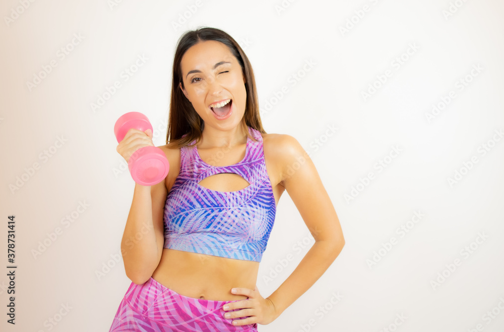Woman in sportswear winking while holding a pink dumbbell Woman in sportswear winking while holding a pink dumbbell