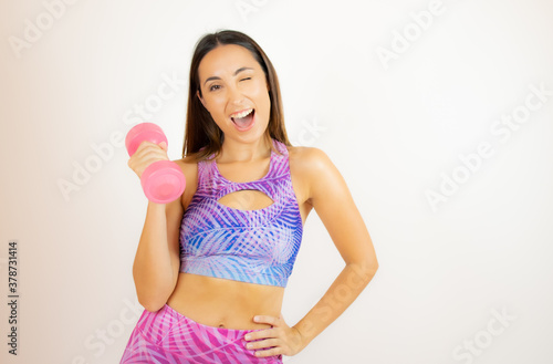 Woman in sportswear winking while holding a pink dumbbell