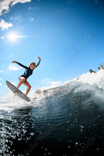 Woman in swimsuit rides on river wave against the background of the blue sky.